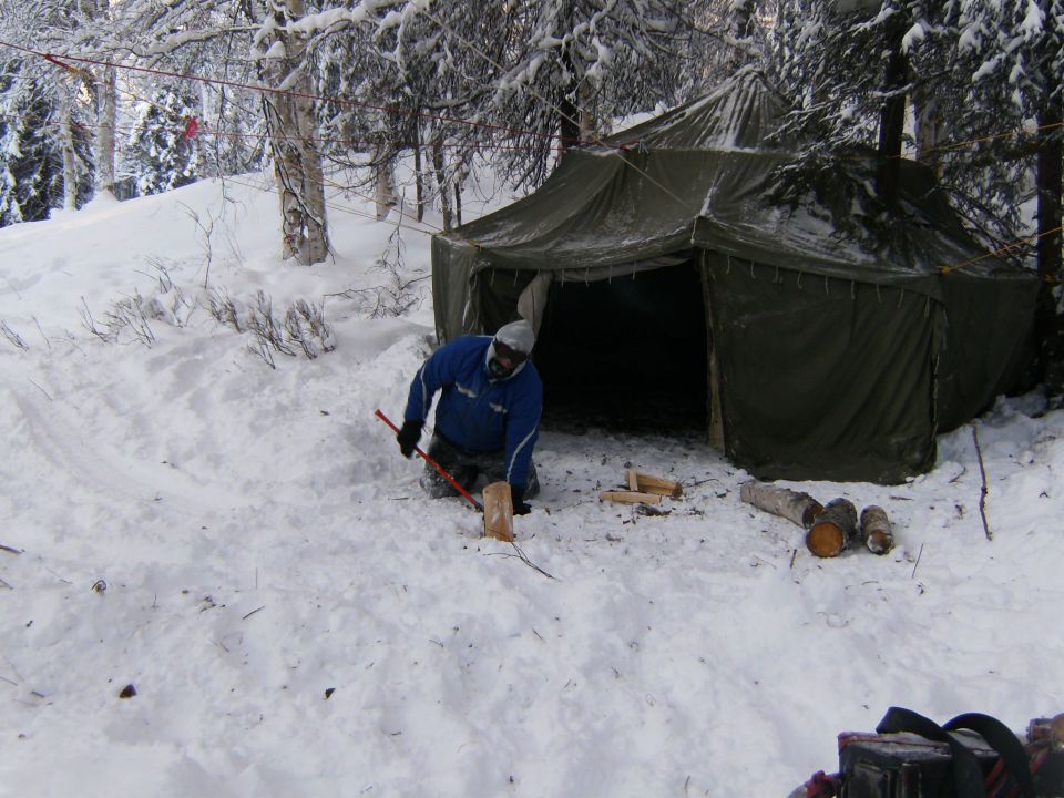 Winter scene with a tent and a person chopping wood