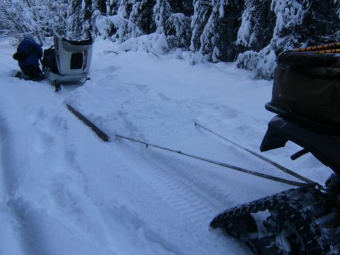2000 Ford E350 - A snowmobile is being towed through a snow-covered forest by a vehicle with tracks visible.