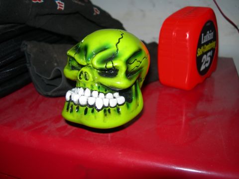 1991 Jeep Wrangler - A custom green skull shift knob sits on a red surface, accompanied by a red tape measure and black fabric.