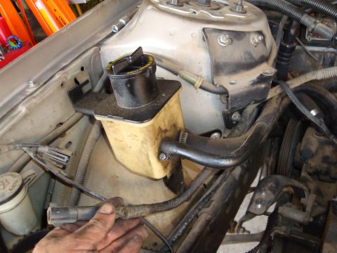 1990 Ford Taurus - The power steering fluid reservoir is visible in this engine bay shot, with a hand reaching for a wire harness.