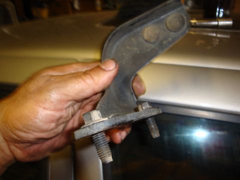 1990 Ford Taurus - A hand holds a car door hinge part against the silver body of a car.