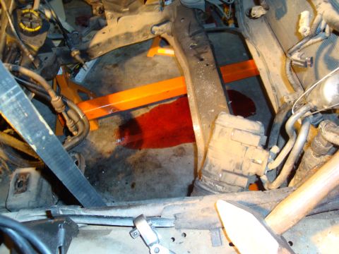 1990 Ford Taurus - A car's engine bay is supported by jack stands, with a significant red fluid leak visible on the concrete floor.