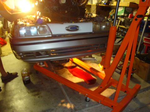 1990 Ford Taurus - A silver 1986 Ford Taurus is suspended by an engine hoist, revealing its engine bay.