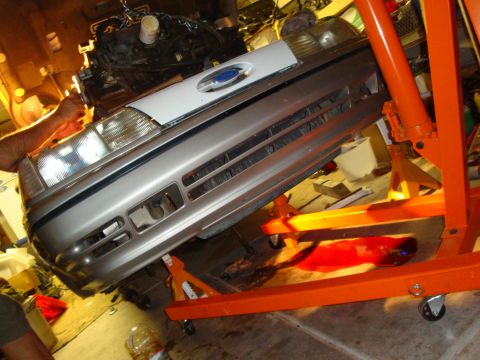 1990 Ford Taurus - The front end of a 1990 Ford Taurus is suspended by an engine hoist, indicating repair or maintenance work.