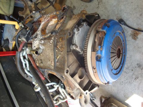 1990 Ford Taurus - Engine block with a blue clutch assembly and a chain hoist attached, suggesting it is being worked on or transported.
