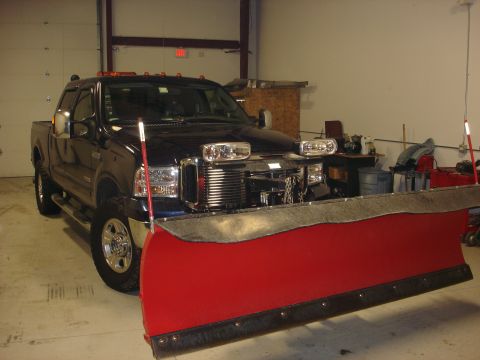 2006 Ford F-350 - A dark blue Ford F-Series truck is parked inside a garage with a large red snow plow mounted on its front end.