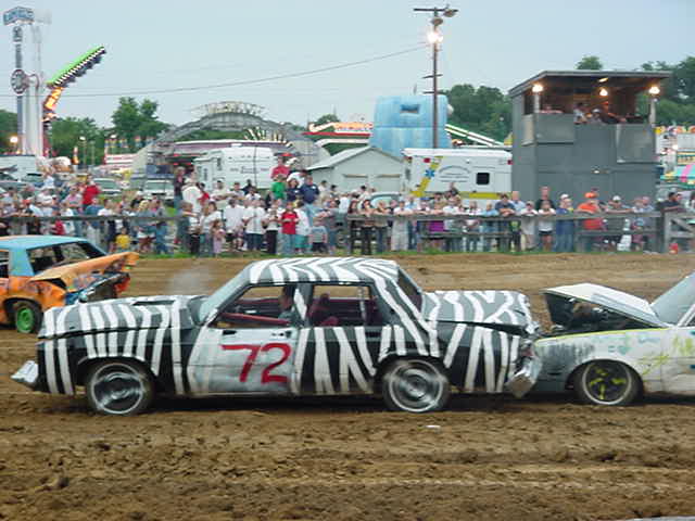 Zebra-painted demolition derby car number 72 colliding with another car in a dirt arena