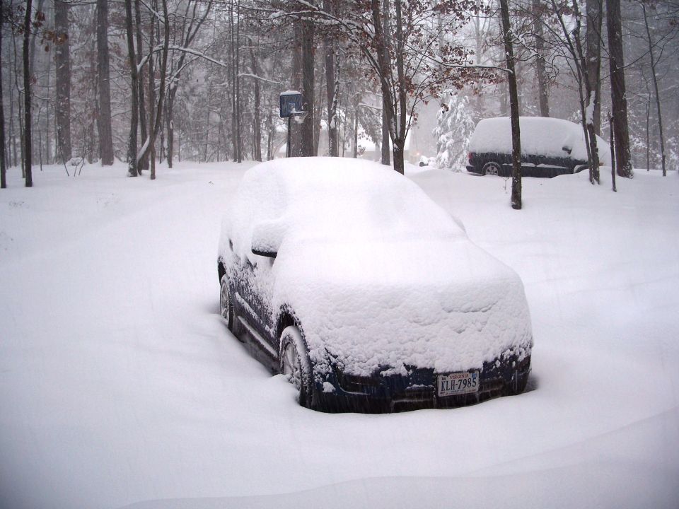 Front view of a dark blue car buried in snow with a license plate visible