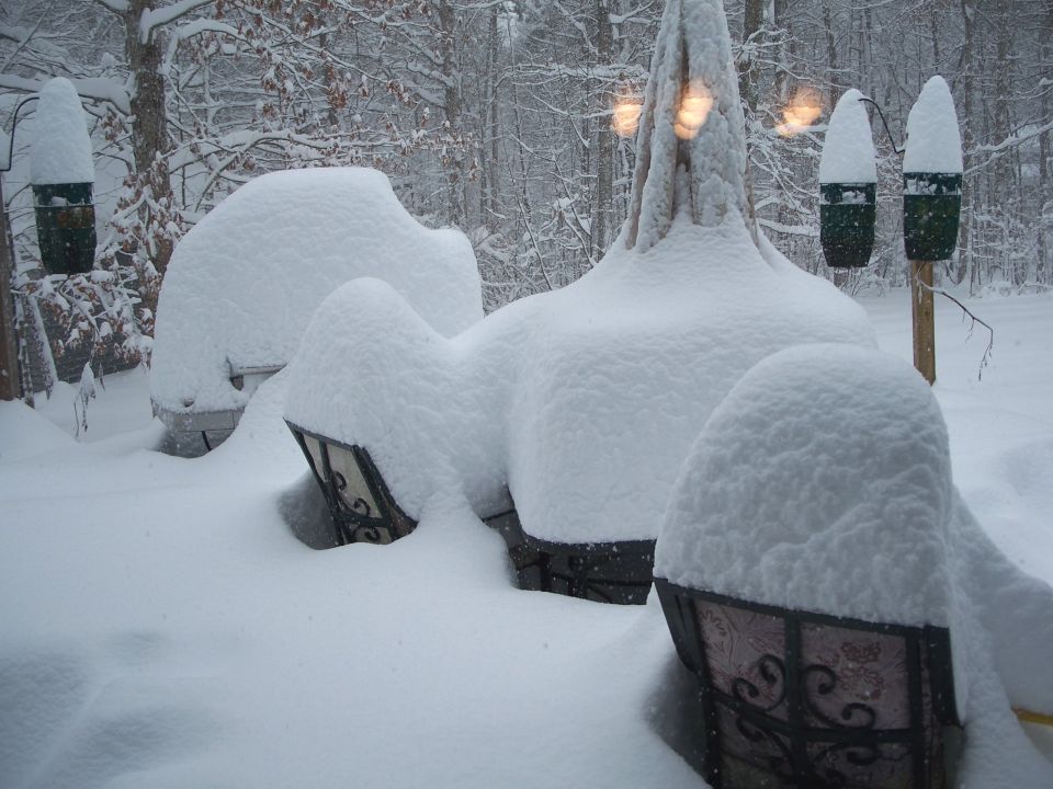 Patio furniture and lanterns buried under deep snow in a wooded yard