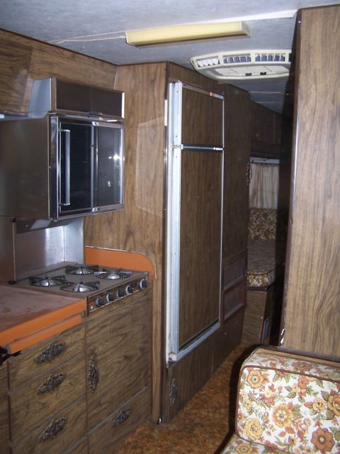 1974 Dodge RV/Conversion Chassis - Interior view of an RV kitchen and living space with wood paneling and floral upholstery.