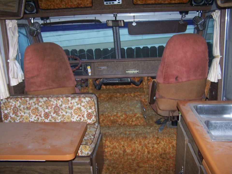 1970s motorhome interior with burgundy captain's chairs, orange shag carpet, dinette and sink