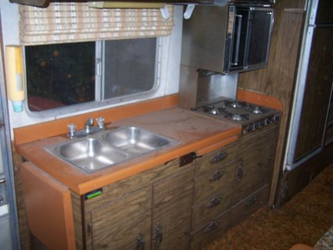 1974 Dodge RV/Conversion Chassis - Interior view of an RV kitchen a sink, stovetop, and wood-paneled cabinets.