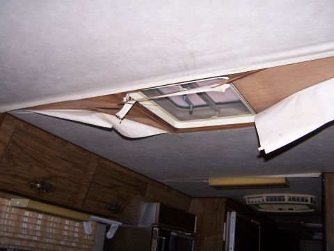 1974 Dodge RV/Conversion Chassis - The interior of an RV shows a damaged ceiling panel peeling away from a skylight, revealing wood paneling and insulation.