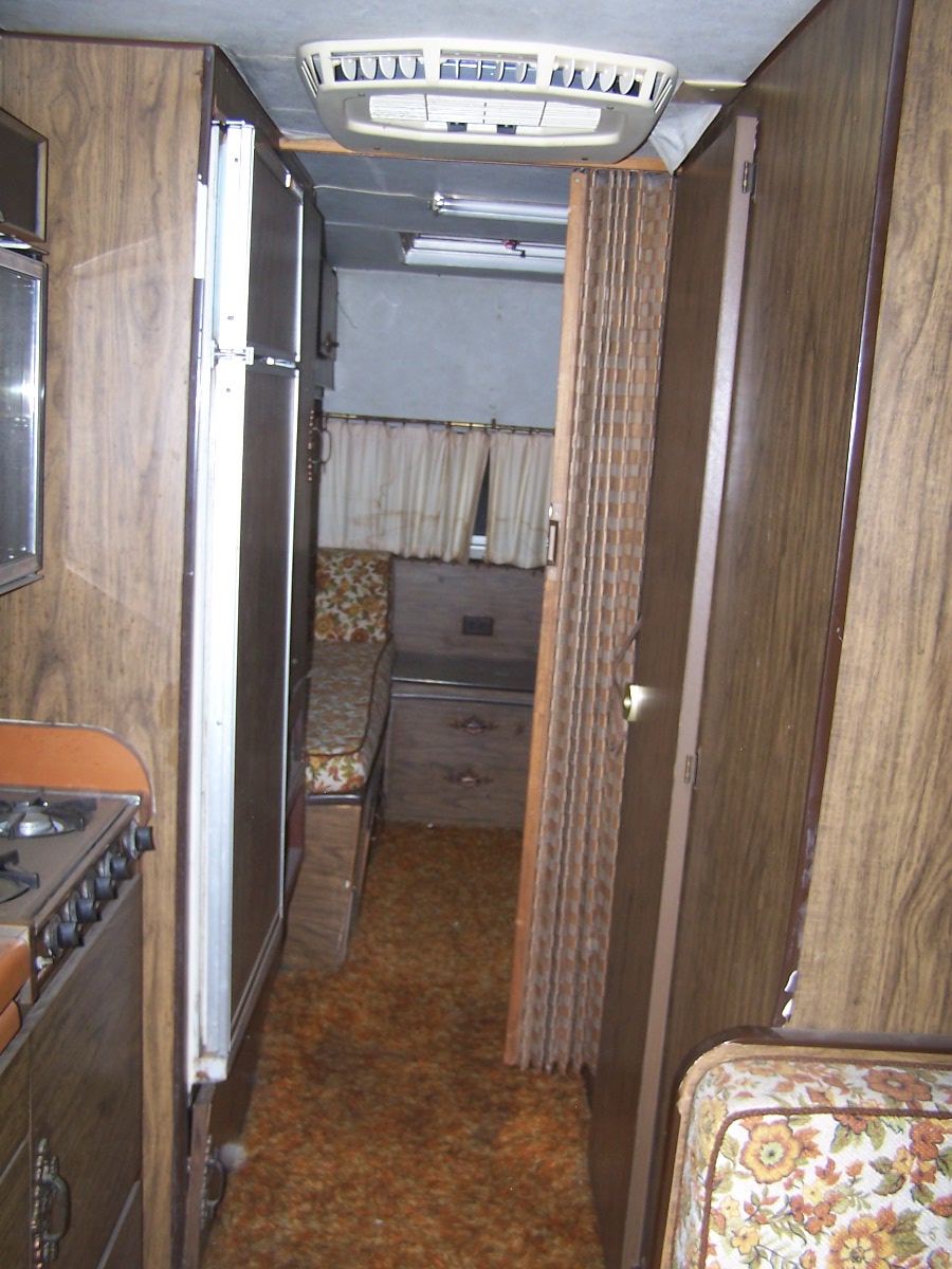 Interior view of an RV showing a refrigerator, stove, seating, and air conditioner