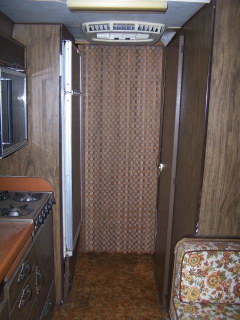 1974 Dodge RV/Conversion Chassis - The interior of this RV features wood paneling, a retro floral couch, and a patterned curtain separating spaces.