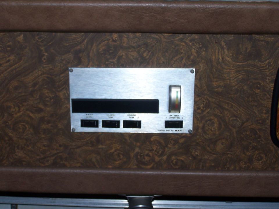 RV tank monitor panel with battery and holding tank gauges on wood-grain wall