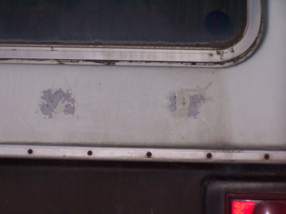 Weathered aluminum RV exterior wall below a window with peeling decal residue