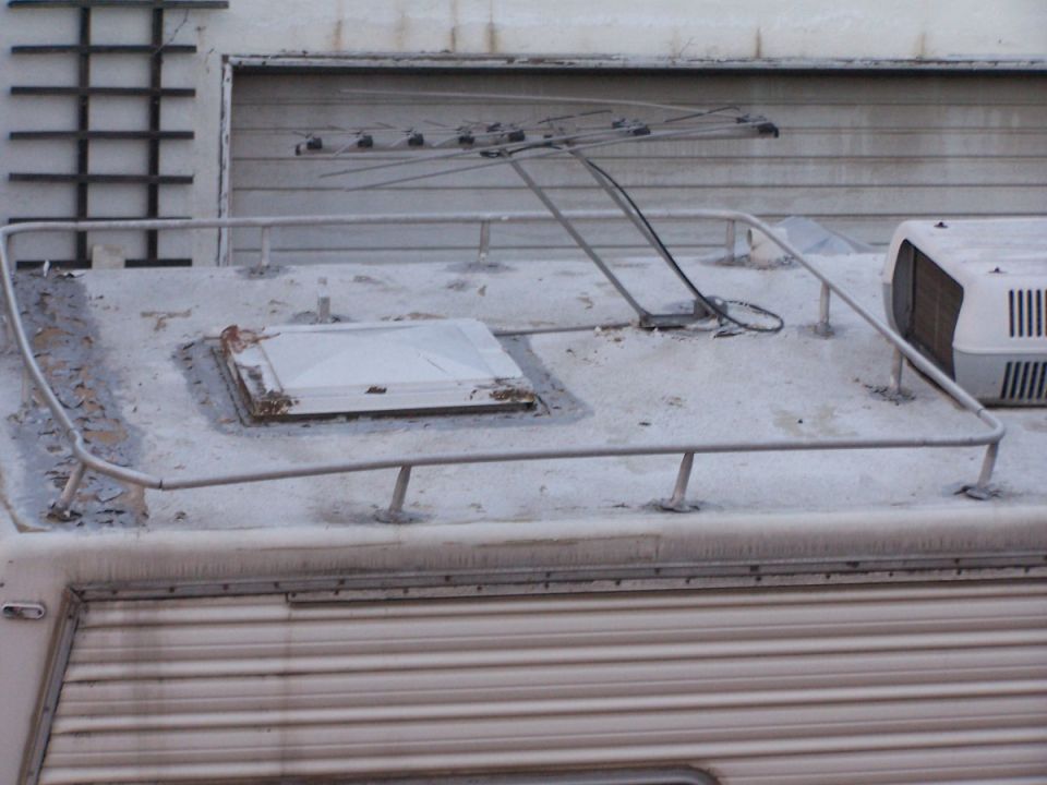 RV roof with antenna, skylight, and AC unit. Side of RV has ribbed paneling