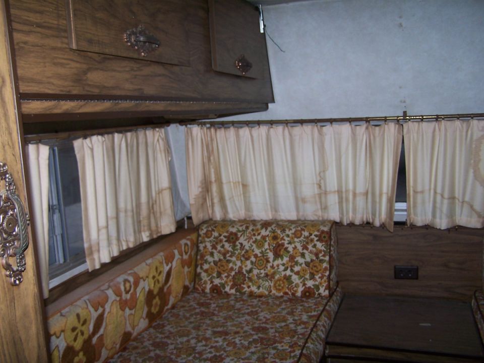 Vintage RV interior with floral couch, cream curtains, and wood cabinets