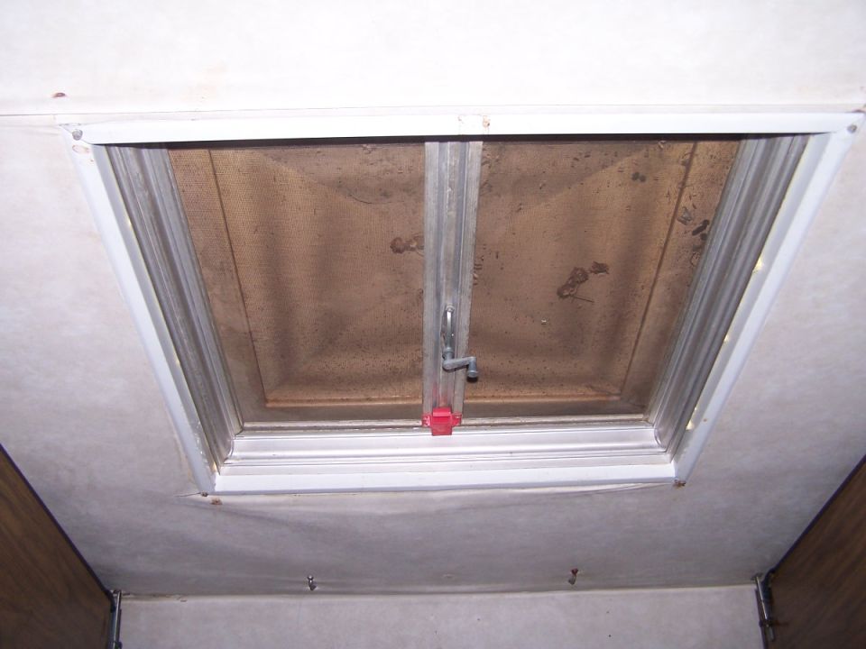 Dirty roof vent hatch with crank handle and red latch in an RV ceiling, seen from below