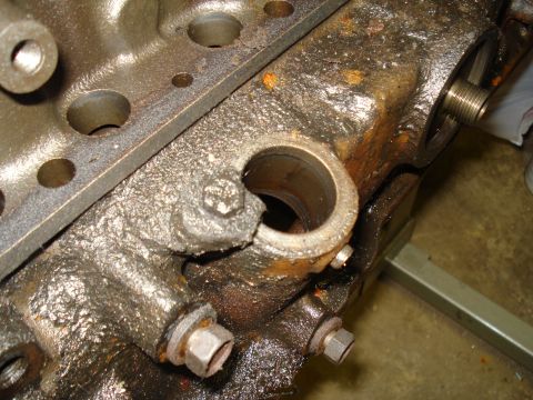 1991 Ford Bronco - This is a close-up view of a heavily soiled engine block, showing a bolt and a threaded opening.