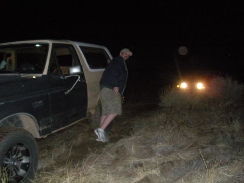 1990 Ford Bronco - A person stands by the open door of a black and tan 1990 Ford Bronco at night, with another vehicle's headlights visible in the distance.