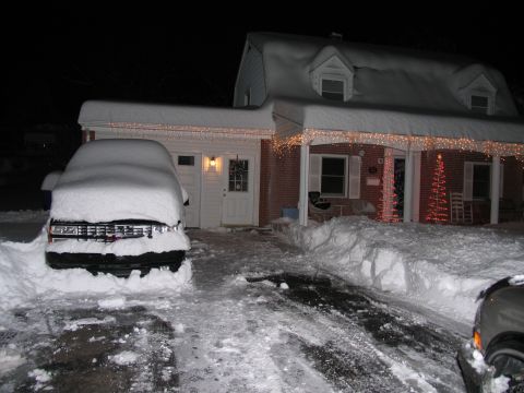 1990 Chevrolet Silverado 1500 - Night shot of a pickup buried under roughly a foot of unbroken snow in a driveway, only its chrome grille, dual round headlights and front…