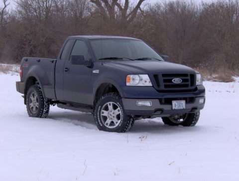 2005 Ford F-150 - A dark blue pickup truck is shown from the front 3/4 view, parked in a snowy field with trees in the background.