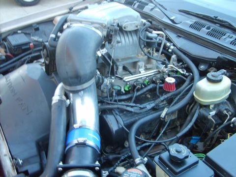 1993 Ford Crown Victoria - Open engine bay of a Ford modular V8 fitted with a bare-aluminum Eaton-style supercharger, a polished mandrel-bent intake tube joined by a…