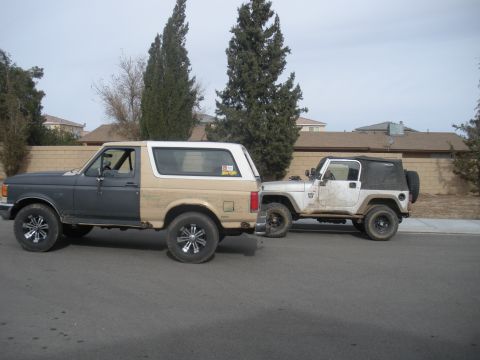 1990 Ford Bronco - A Ford Bronco and a Jeep Wrangler are parked side-by-side on a residential street.