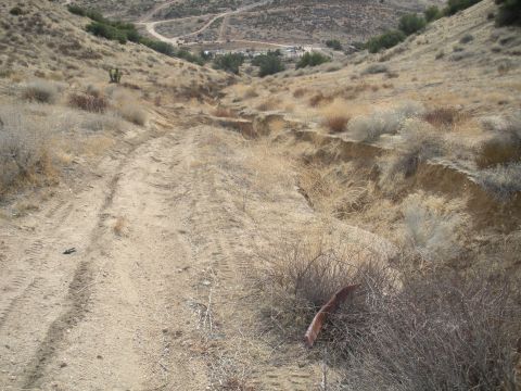 1990 Ford Bronco - A dirt road winds through a dry, eroded hillside, showing tire tracks from off-road travel.
