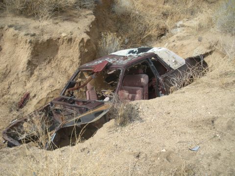 1990 Ford Bronco - This heavily damaged vehicle is lodged in a dirt embankment, its interior exposed to the elements.