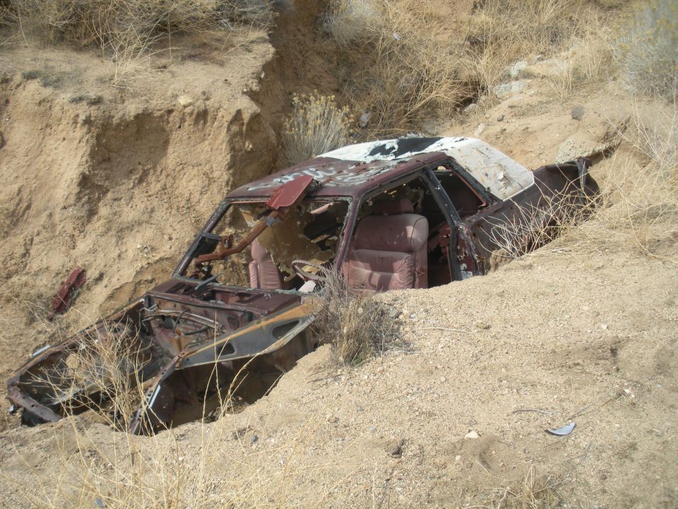 Wrecked maroon car with white roof, interior visible, stuck in dirt embankment