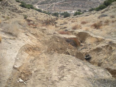 1990 Ford Bronco - A tire lies in a ditch on a dry, eroded hillside. Supermotors.net logo is visible.
