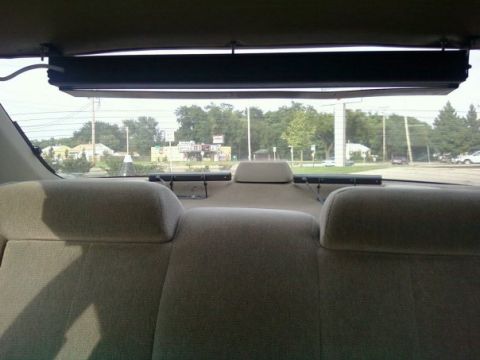 2000 Mercury Grand Marquis - View from the rear interior of a vehicle, looking out the back window at a suburban landscape.