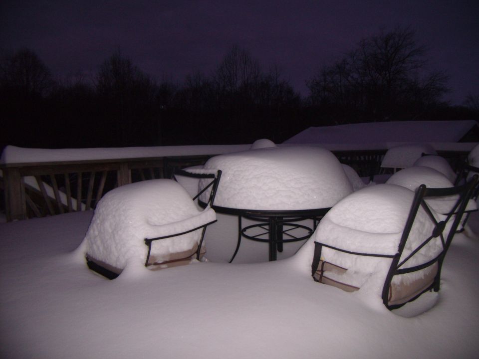 Patio chairs and table covered in snow on a deck at dusk