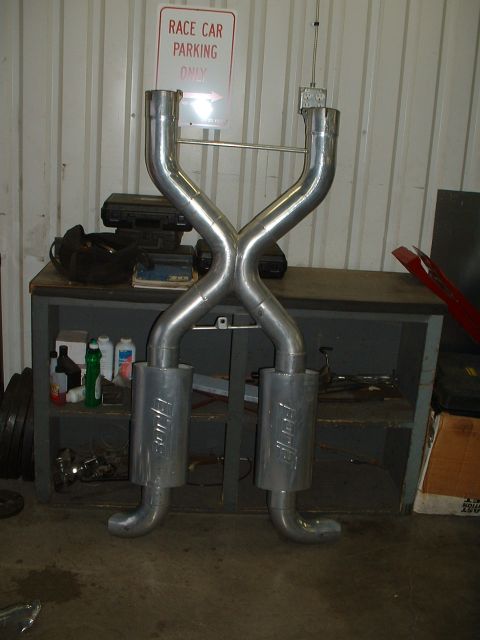 1963 Ford Fairlane - An X-pipe exhaust system with two mufflers is displayed in a workshop, with a 'Race Car Parking Only' sign in the background.