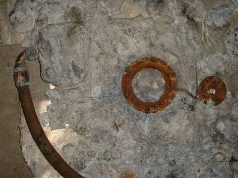 1963 Ford Fairlane - Close-up of a corroded pipe fitting and cap on a textured concrete wall.