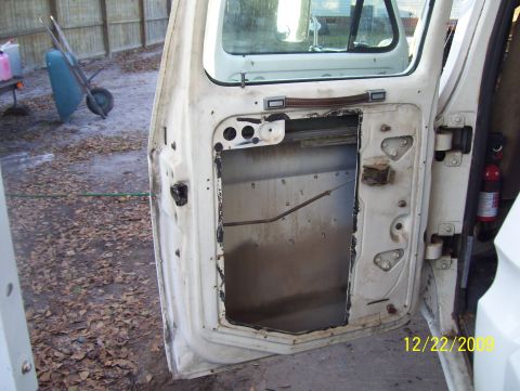 1978 Ford Bronco - The interior of a white vehicle door shows exposed metal and wiring, with a fire extinguisher mounted on the right.
