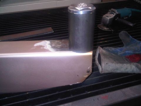 1996 Ford Bronco - Metal fabrication setup with a part, cap, grinder, and glove on a work surface.
