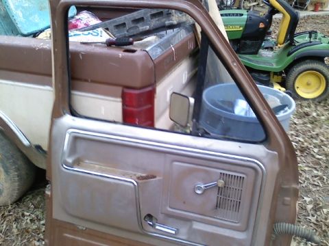 1990 Ford Bronco - A side view of a brown and white Ford pickup truck's interior door panel and bed, with a lawnmower visible behind it.