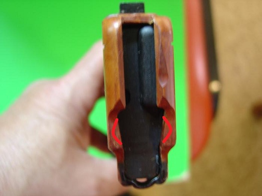 Wooden gun grip with red markings, held by a hand against a green background