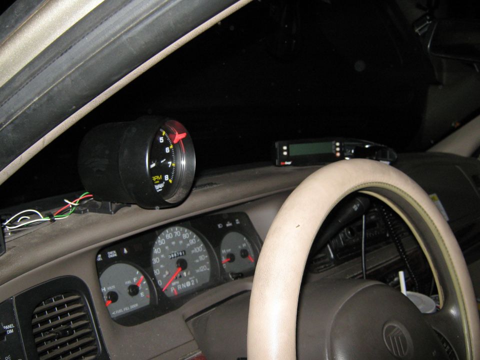 Dashboard interior with a black tachometer mounted above the instrument cluster and a digital display unit behind the steering wheel