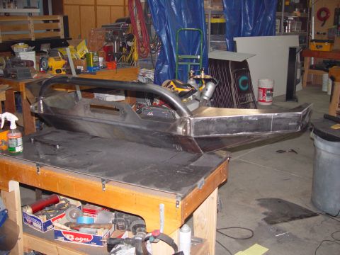 1993 Ford Bronco - Custom metal bumper with roll cage hoop sits on a workbench in a garage.