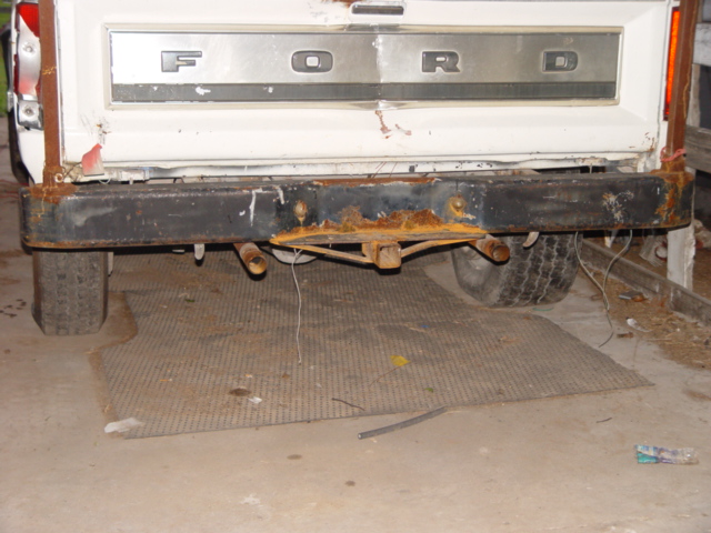 Ford tailgate with chrome trim and rusted black bumper. Trailer hitch visible