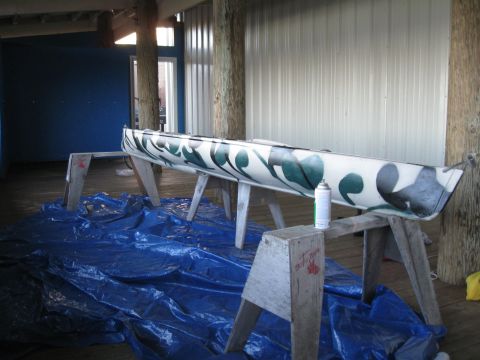 1991 Ford Bronco - A canoe is being painted with a camouflage pattern while resting on sawhorses indoors.