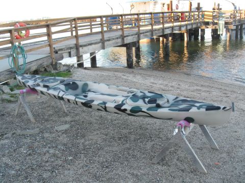 1991 Ford Bronco - A camouflage kayak rests on stands near a wooden pier and the water's edge.