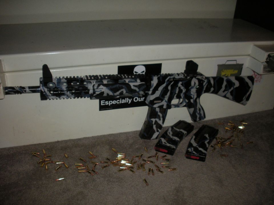 Assault rifle with black and white camouflage pattern, two magazines, and scattered ammunition on a carpeted surface