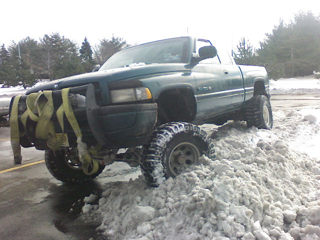Green 1998 Dodge 1500 stuck in snow, front end visible with yellow straps