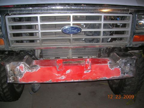 1985 Ford Bronco - Close-up of the front grille and bumper of a 1985 Ford Bronco, showing a red bumper with signs of repair.
